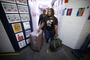 Two women carrying a bag and rolling a suitcase through a dorm hallway_Photo by Dan Z. Johnson