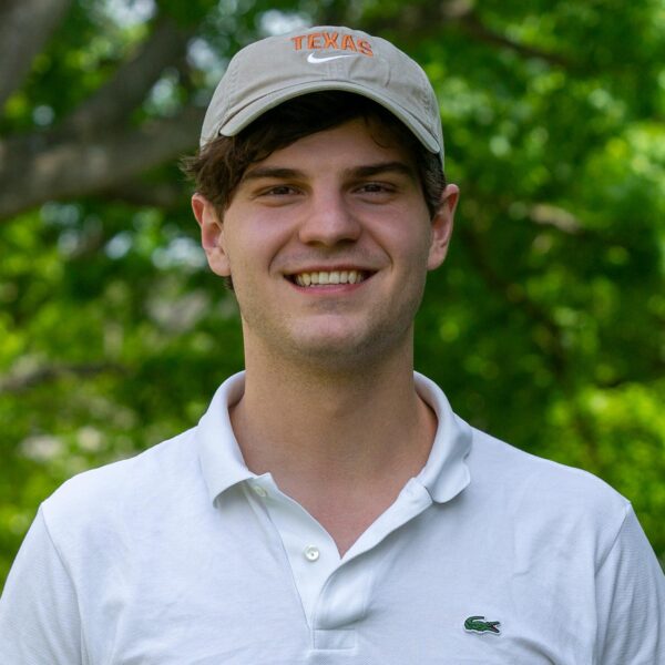 Filip Kesicki, wearing a white shirt and grey cap, stands against and out-of-focus arboretum bacground