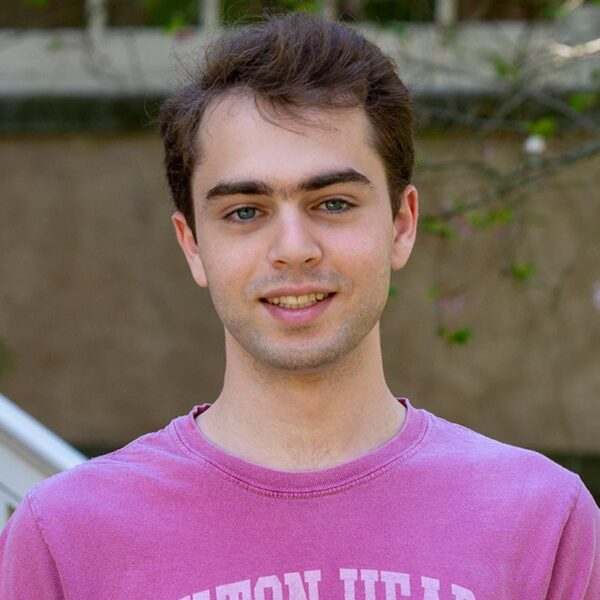 Nicholas Bayan Mostaghim wears a pnink shirt in a portrait taken in front of a historic building on Haverford's campus.