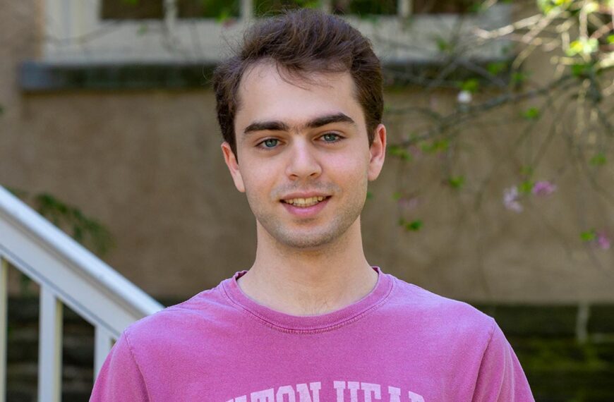 Nicholas Bayan Mostaghim wears a pnink shirt in a portrait taken in front of a historic building on Haverford's campus.