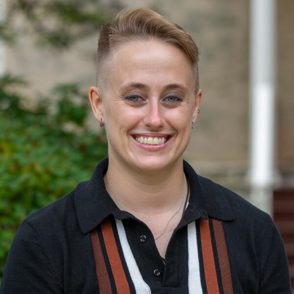 A portrait of Katie (kt) Tedesco, who wears a dark, collared shirt with stripes.
