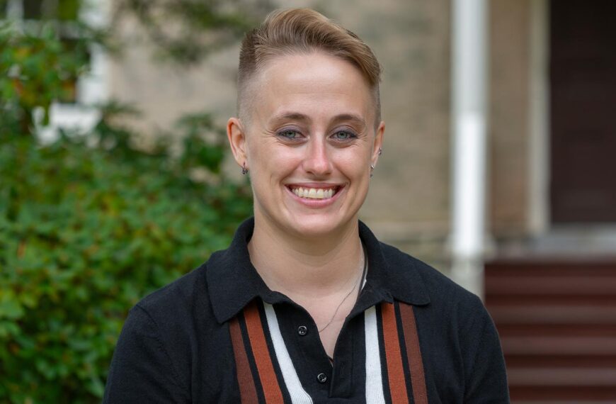 A portrait of Katie (kt) Tedesco, who wears a dark, collared shirt with stripes.