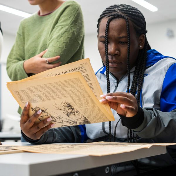 A student sits at a table and looks over a folded piece of aged paper from Temple University's archives.