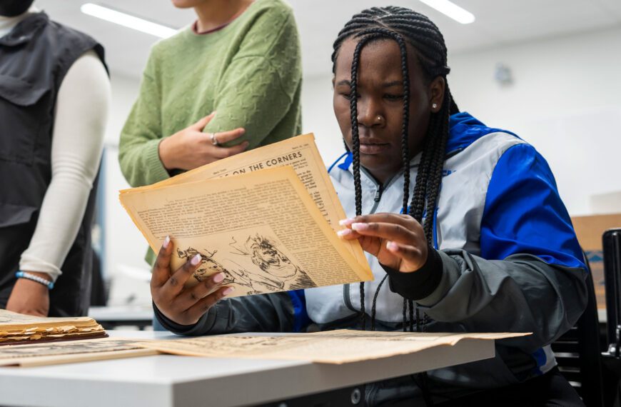 A student sits at a table and looks over a folded piece of aged paper from Temple University's archives.