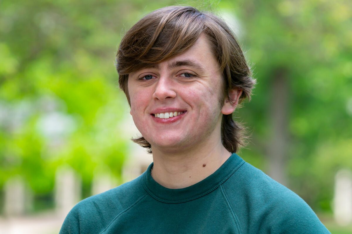 Charlie Crawford smiles in a portrait. He is pictured against an out-of-focus backdrop on Haverford's lush campus.
