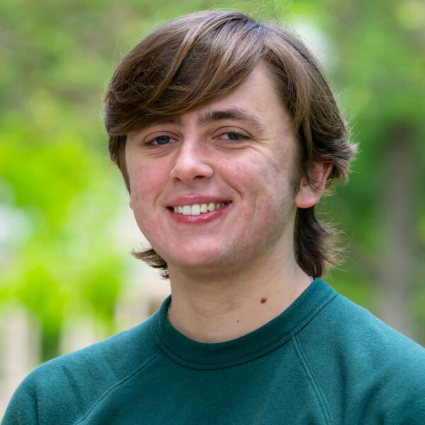 Charlie Crawford smiles in a portrait. He is pictured against an out-of-focus backdrop on Haverford's lush campus.