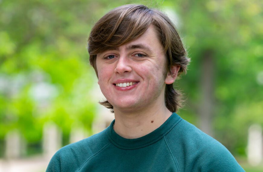 Charlie Crawford smiles in a portrait. He is pictured against an out-of-focus backdrop on Haverford's lush campus.