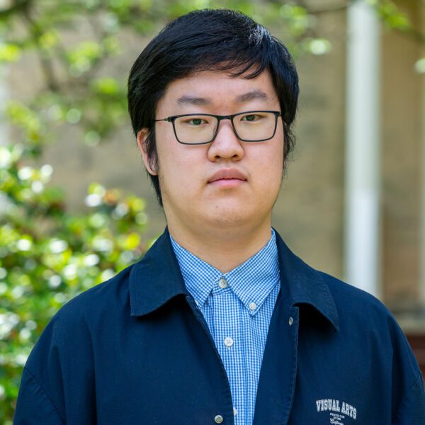 Jian Wei wears a blue shirt and navy jacket in a portrait taken against one of Haverford's historic buildings.