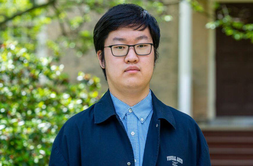 Jian Wei wears a blue shirt and navy jacket in a portrait taken against one of Haverford's historic buildings.