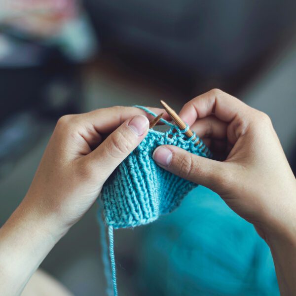 Two hands hold knitting needles as a person works on a knitting project.