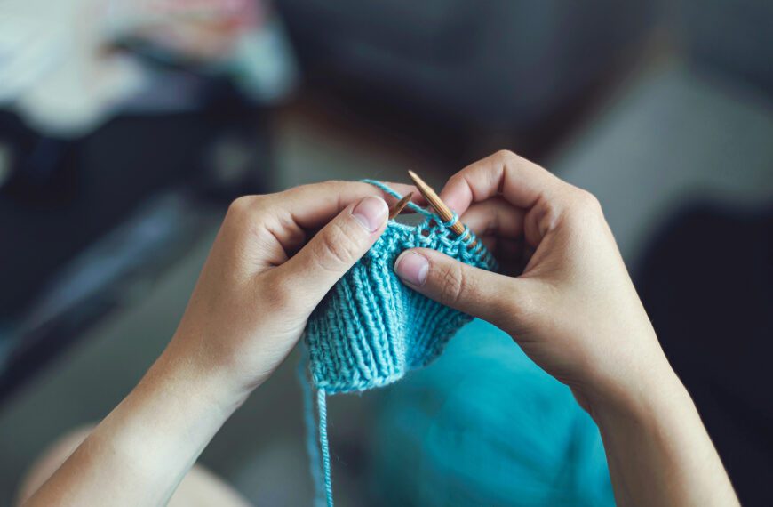 Two hands hold knitting needles as a person works on a knitting project.