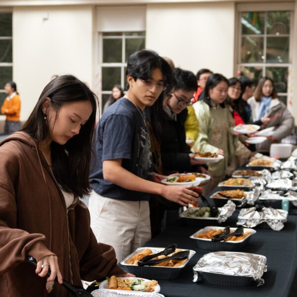 Students stand in a line to serve themselves food from a buffet lined up on several tables.