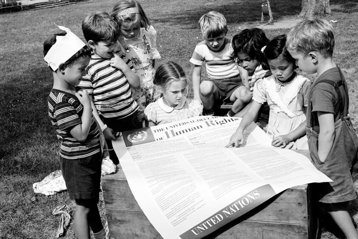 Eight children gather around a large printed copy of the U.N.'s Universal Declaration of Human Rights.