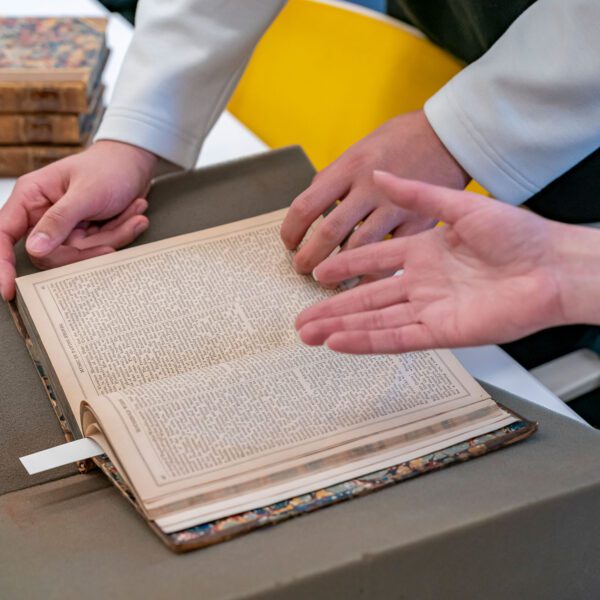 Two students, with only their hands visible, inspect a very old book contained within Haverford's special collections.