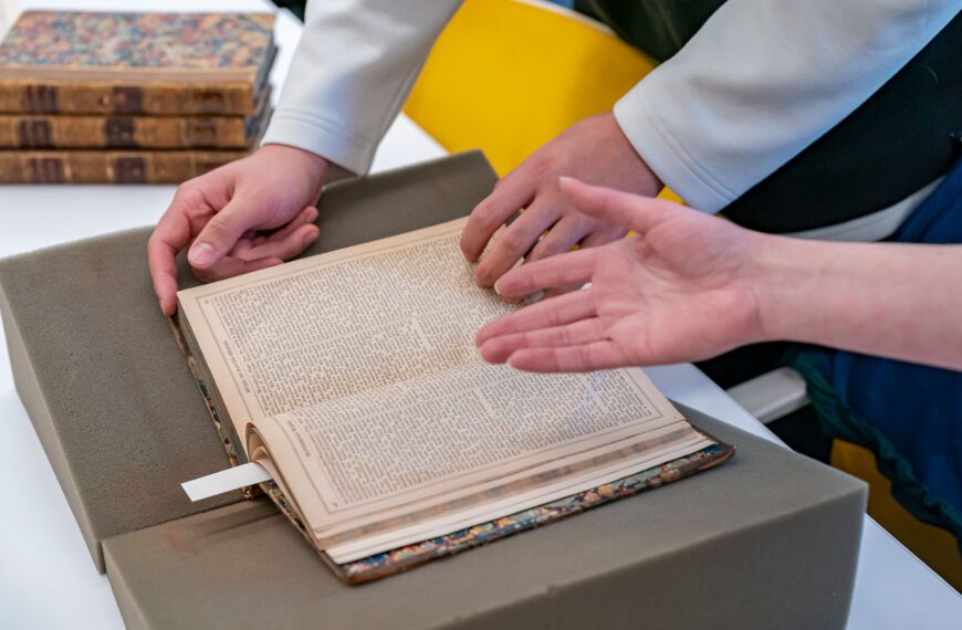 Two students, with only their hands visible, inspect a very old book contained within Haverford's special collections.