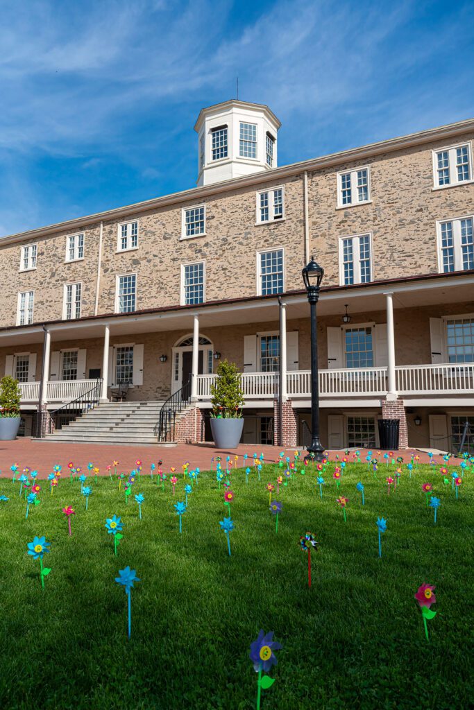 Founders Hall rises behind a lawn planted with colorful pinwheels under a vivid blue sky.