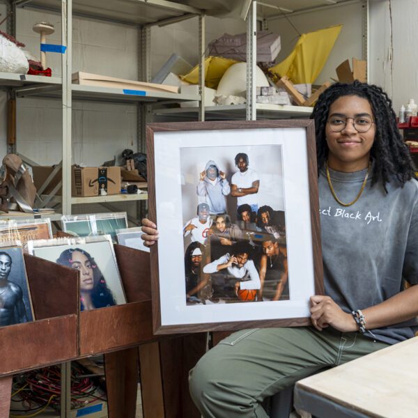 Ella Mbanefo ’26 sits in a studio holding a framed photograph, with shelves of art materials and bins of vinyl records behind her.