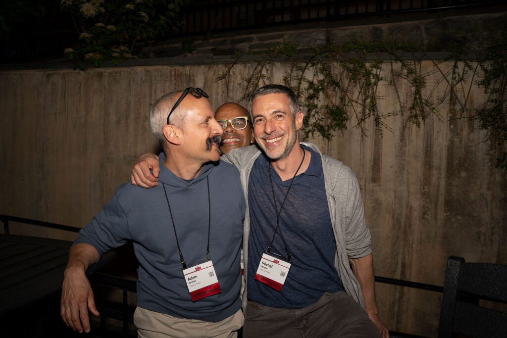 Three alumni wearing reunion name tags smile and pose together outdoors during an evening reception.