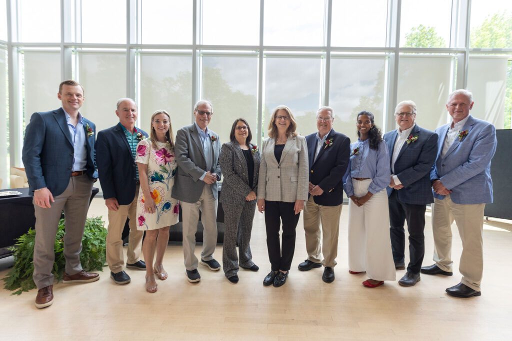 A group of honorees and presenters stand together in a bright room with tall windows during an Alumni Awards gathering.