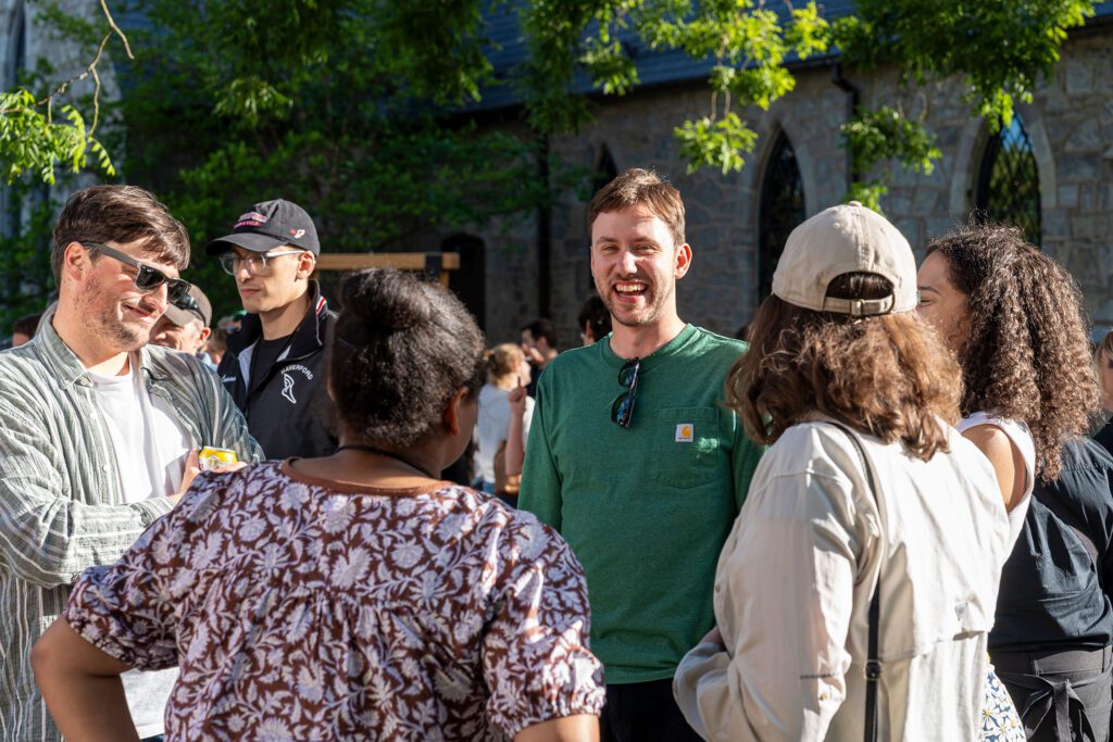 A small group of alumni stands in conversation outdoors, smiling and talking in the late-day sun.
