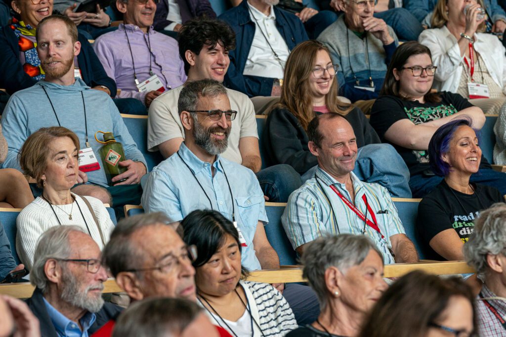 Audience members seated in a tiered lecture hall smile and listen during a forum session.